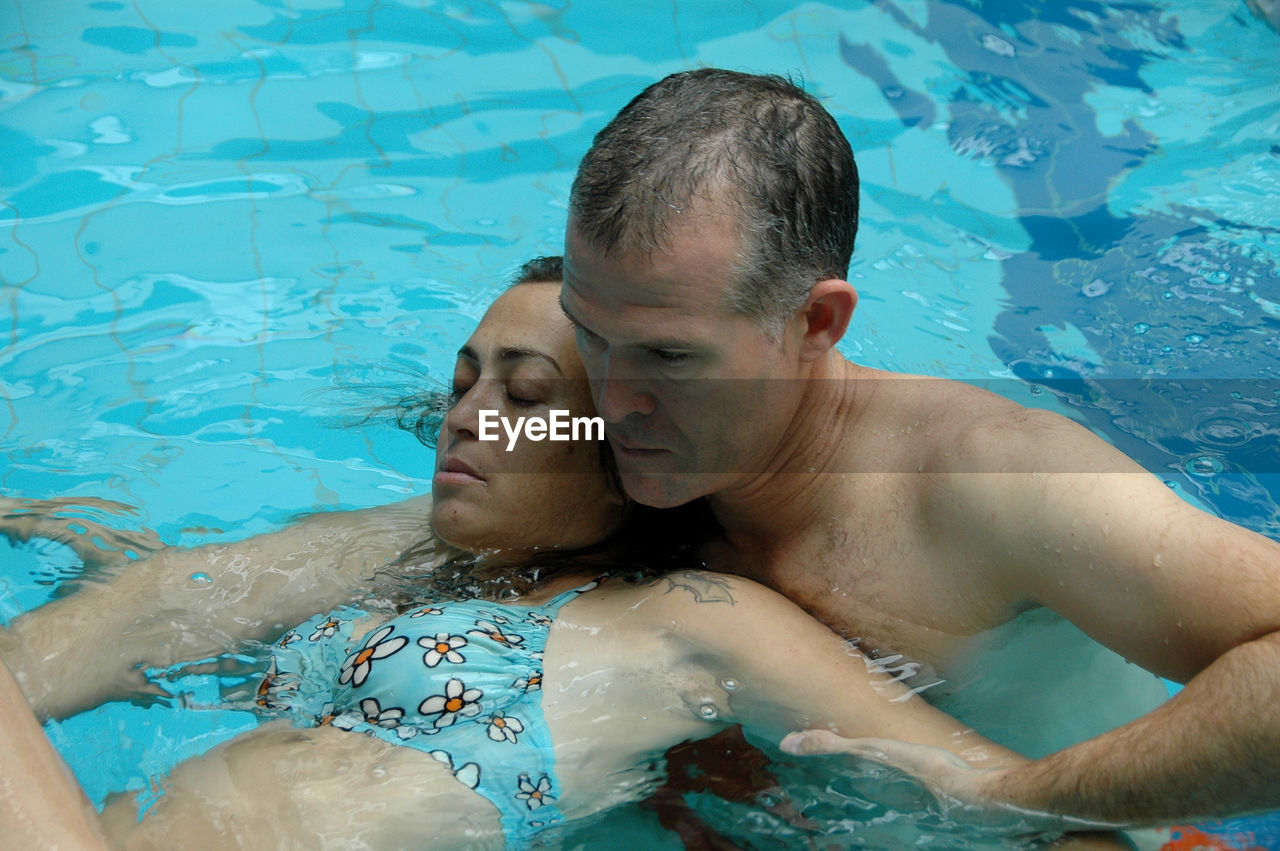 High angle view of mature man teaching young daughter swimming in pool