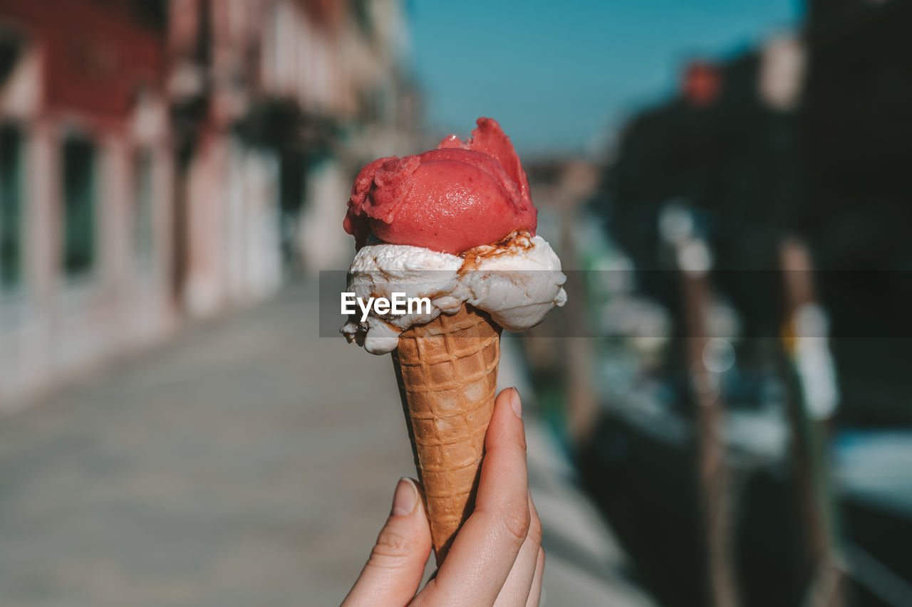 Cropped hand holding ice cream cone in city