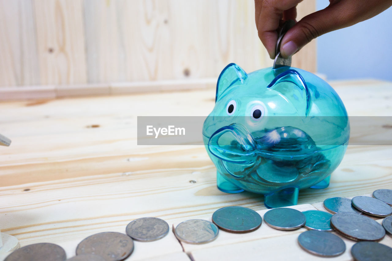 Person holding coin over piggy bank on wooden table