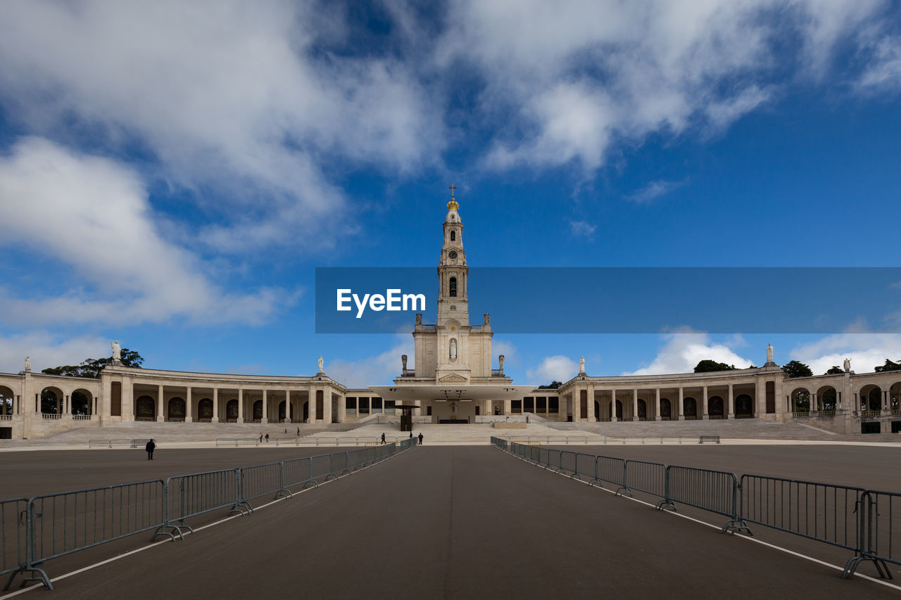 Road leading towards bell tower against cloudy sky