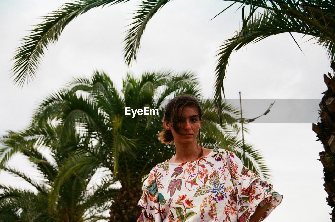 young woman standing against palm trees