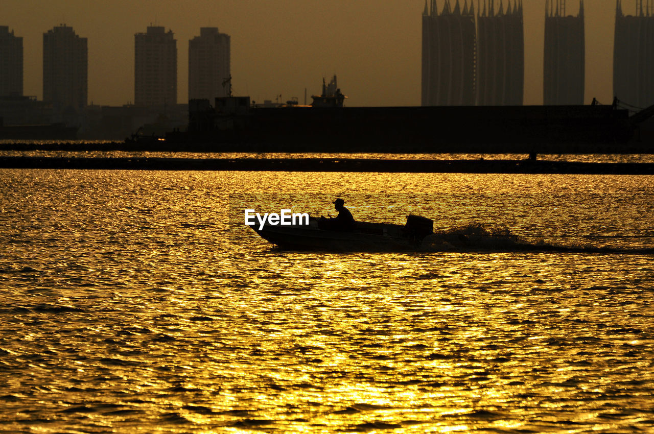 Silhouette man in boat on river by city during sunset