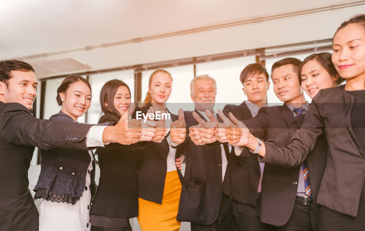 Business people showing thumbs up while standing in office