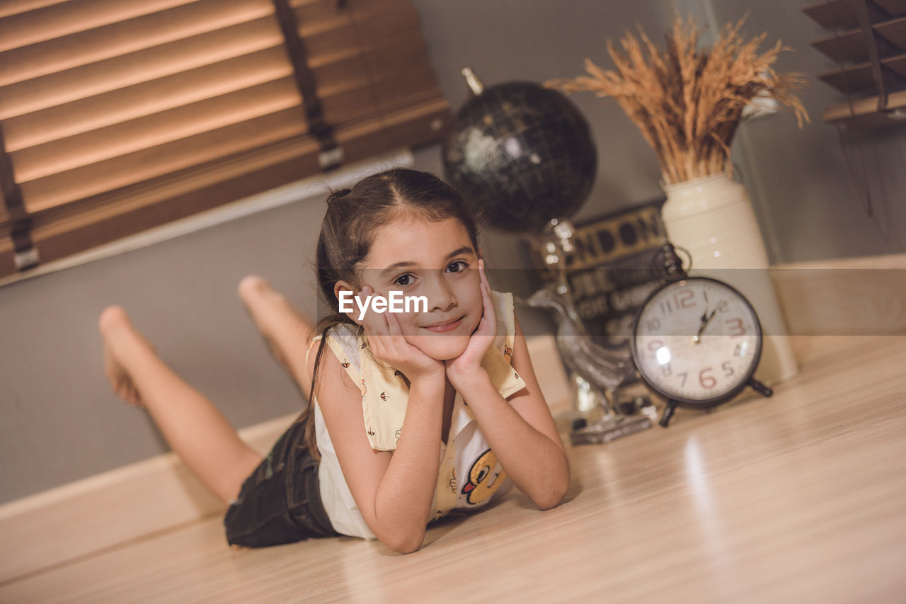 Full length portrait of cute smiling girl lying on floor at home