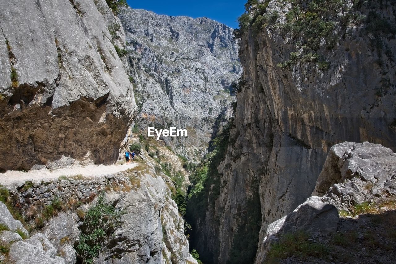 Mid distance of people walking on trail amidst rocky mountains