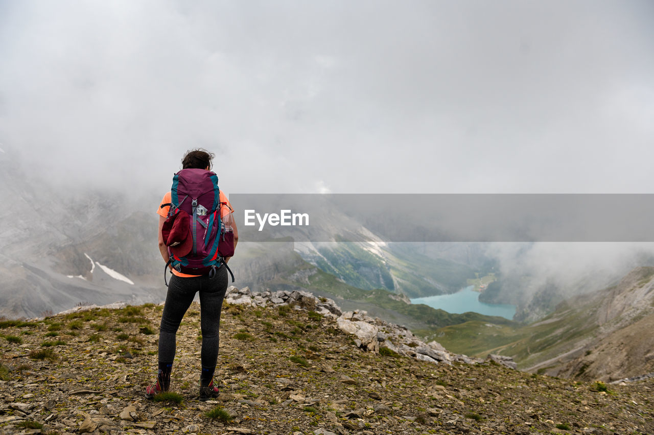 REAR VIEW OF MAN LOOKING AT MOUNTAIN RANGE