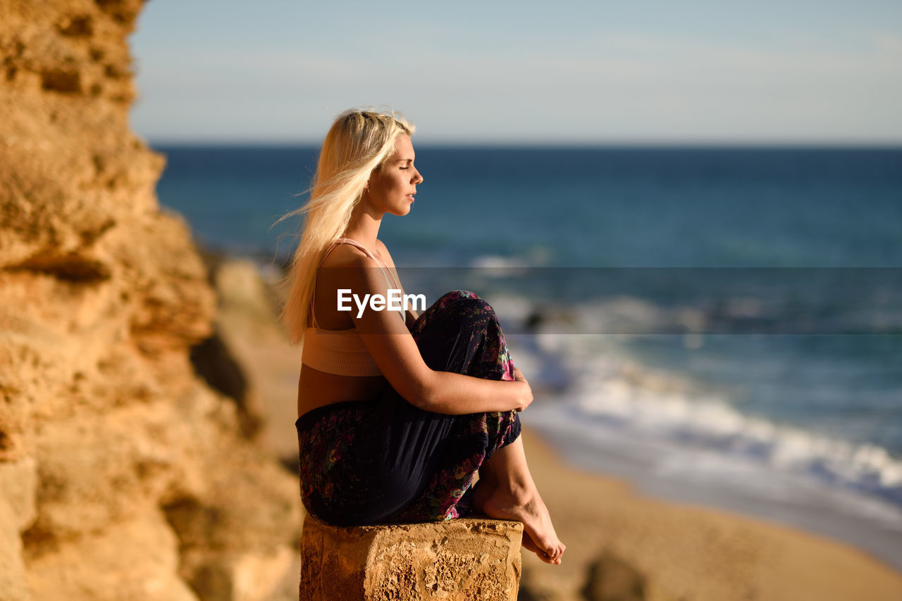 Side view of young woman with eyes closed sitting at beach