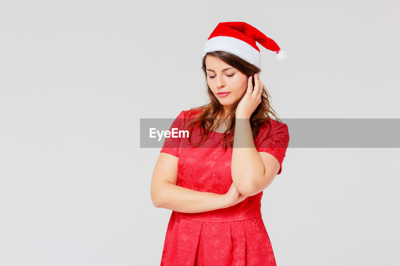 Shy young woman wearing santa hat while standing against gray background