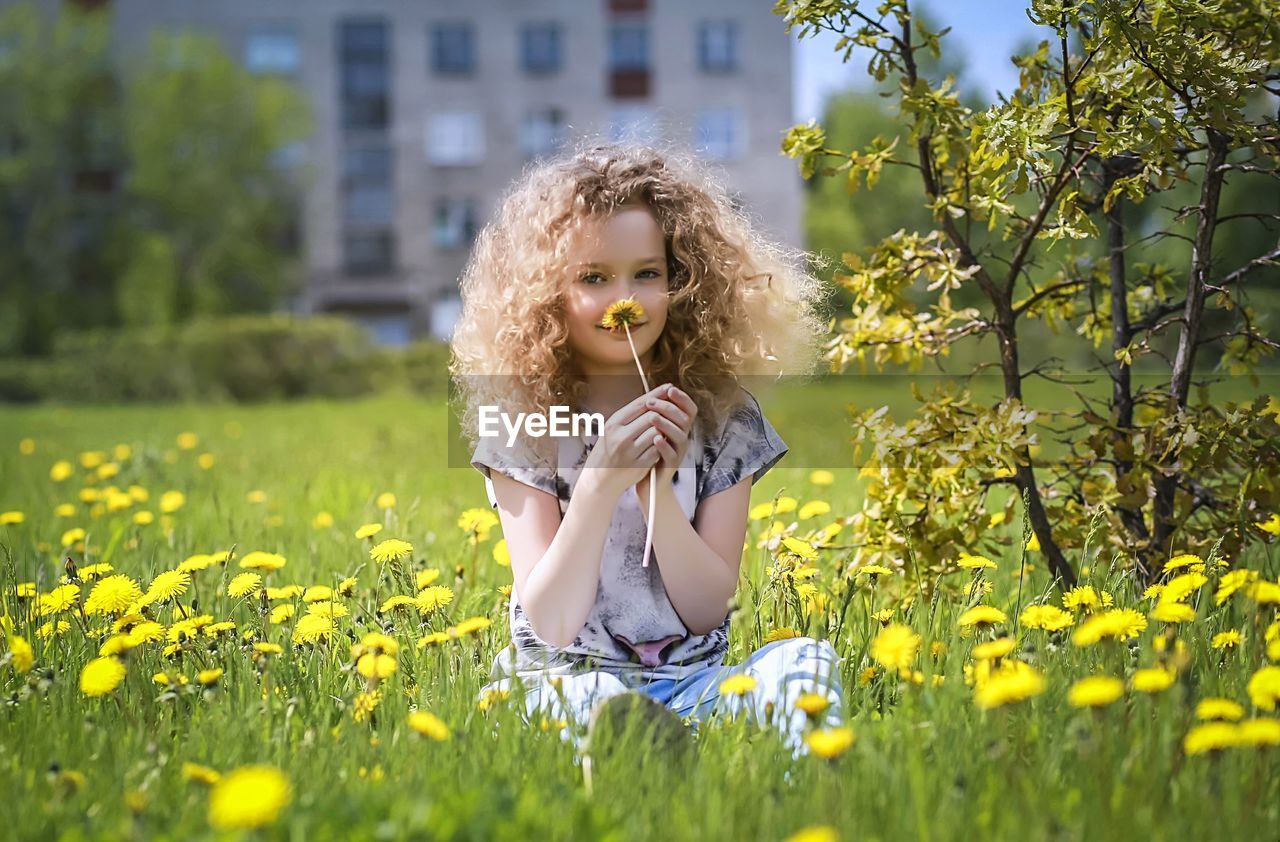 Portrait of cute girl smelling flower while sitting on grassy field