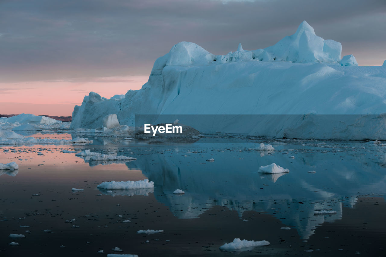 Iceberg in sea against cloudy sky during sunset