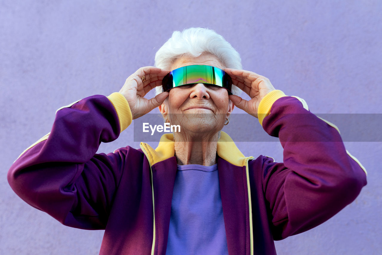 Cheerful elderly female athlete with gray hair in sportswear and blindfold on violet background