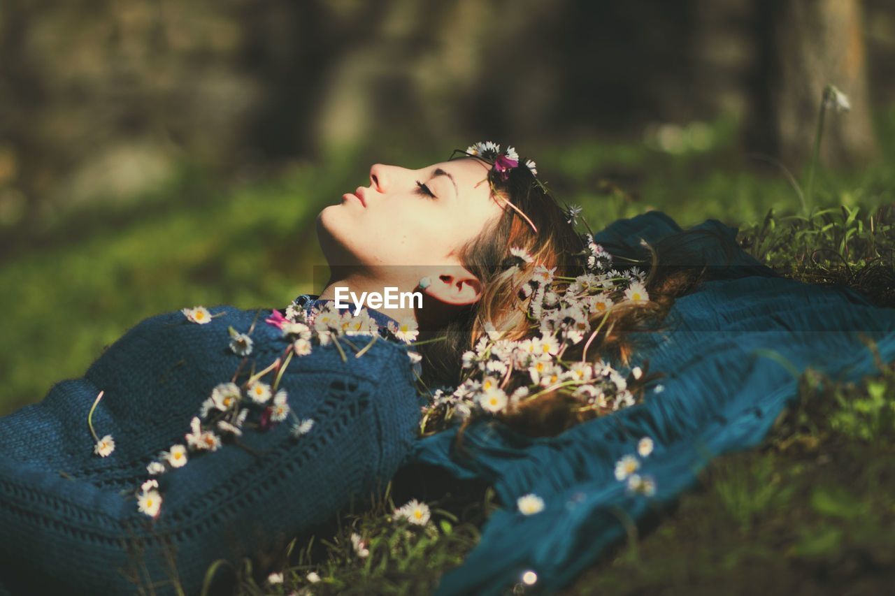 Young woman with flowers lying down on field