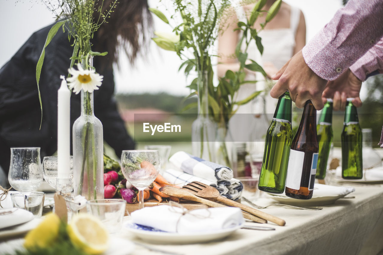 Cropped image of man holding beer bottles at dining table during dinner party in backyard