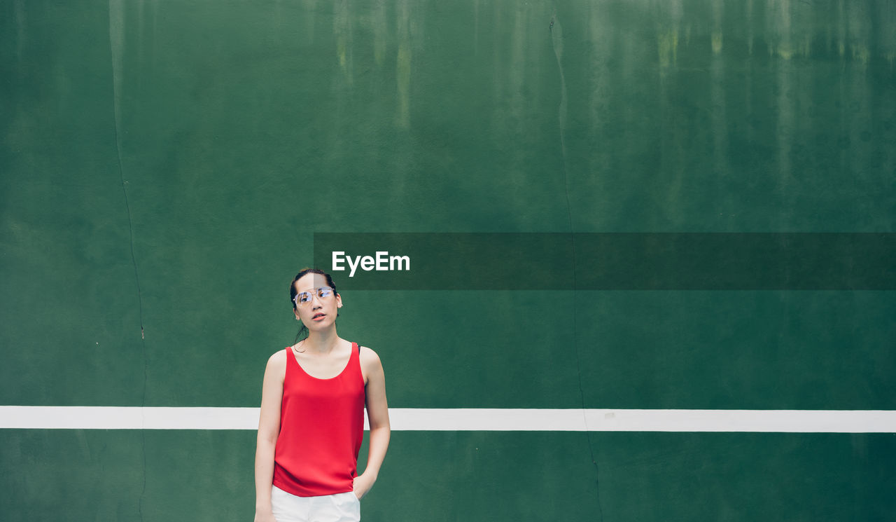 Woman wearing eyeglasses while standing against wall