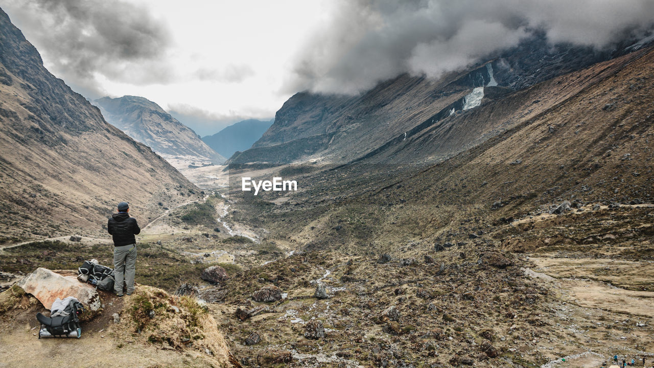 Rear view of man standing on mountain against cloudy sky