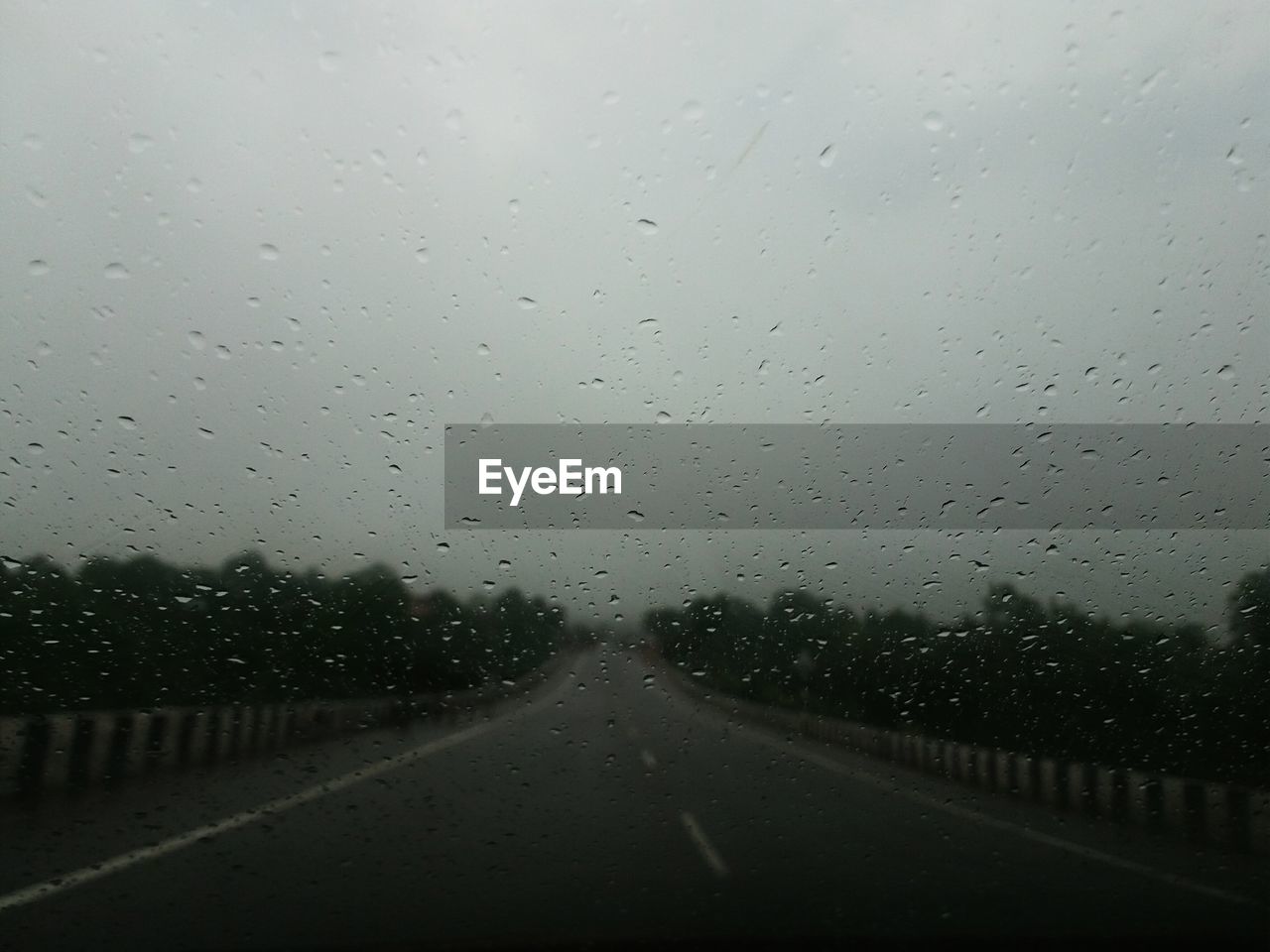 Road seen through wet glass window of car