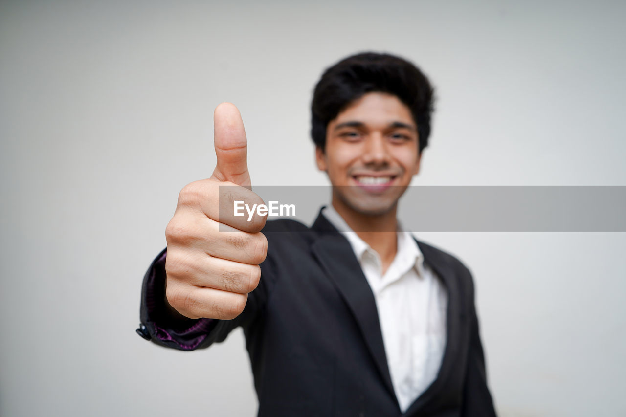 Portrait of businessman showing thumbs up against white background