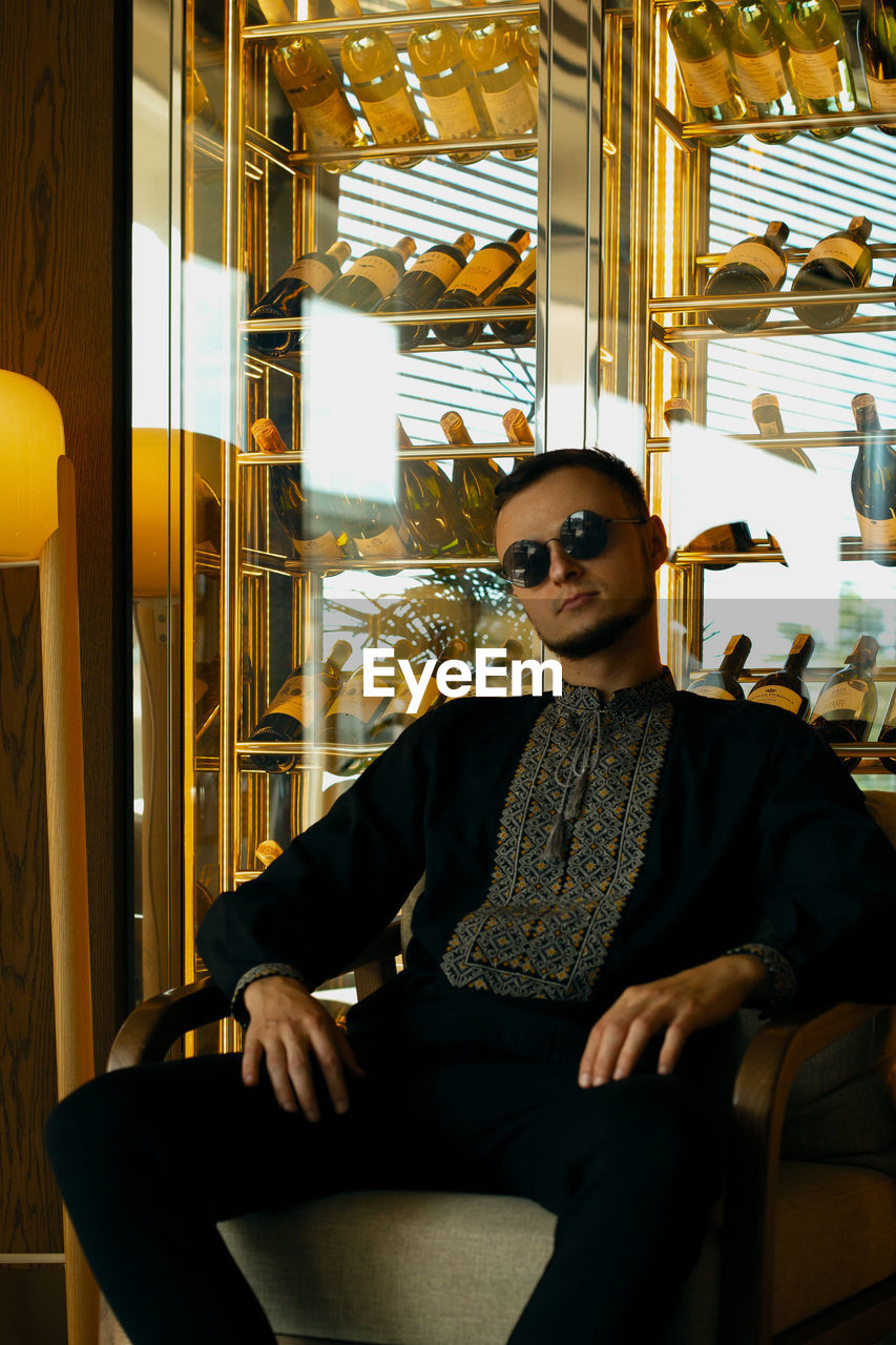 fashion, one person, sitting, adult, glasses, sunglasses, indoors, business, three quarter length, portrait, men, young adult, yellow, clothing, person, seat, chair, looking at camera, luxury, front view, wealth, cool attitude, eyeglasses