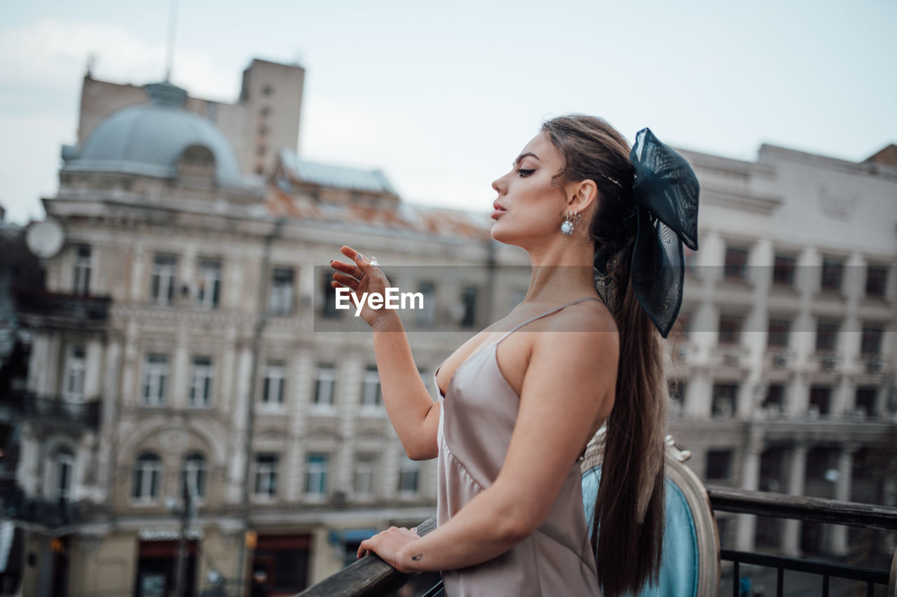 Side view of young woman standing against buildings in city