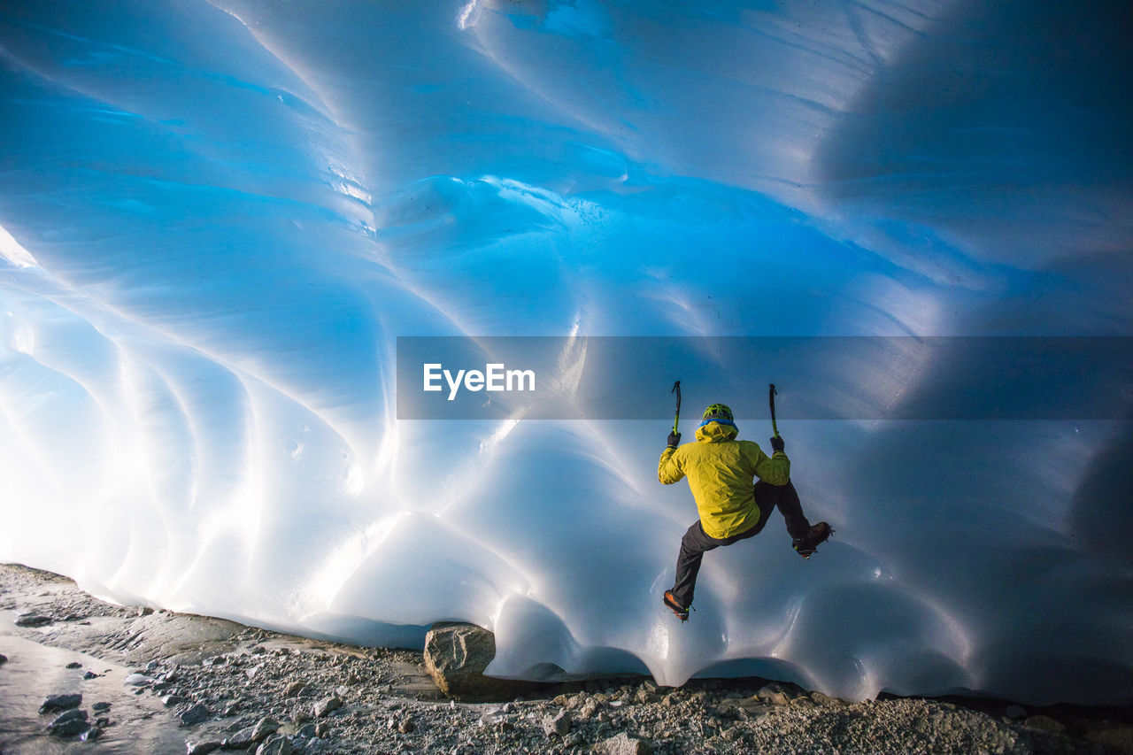 Mountaineer ice climbing on glacial ice in ice cave.