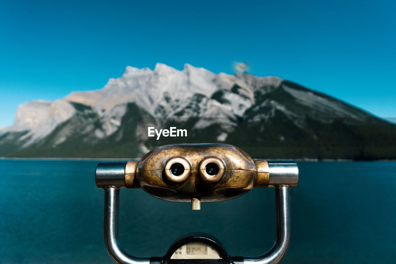 Close-up of coin-operated binoculars against mountains