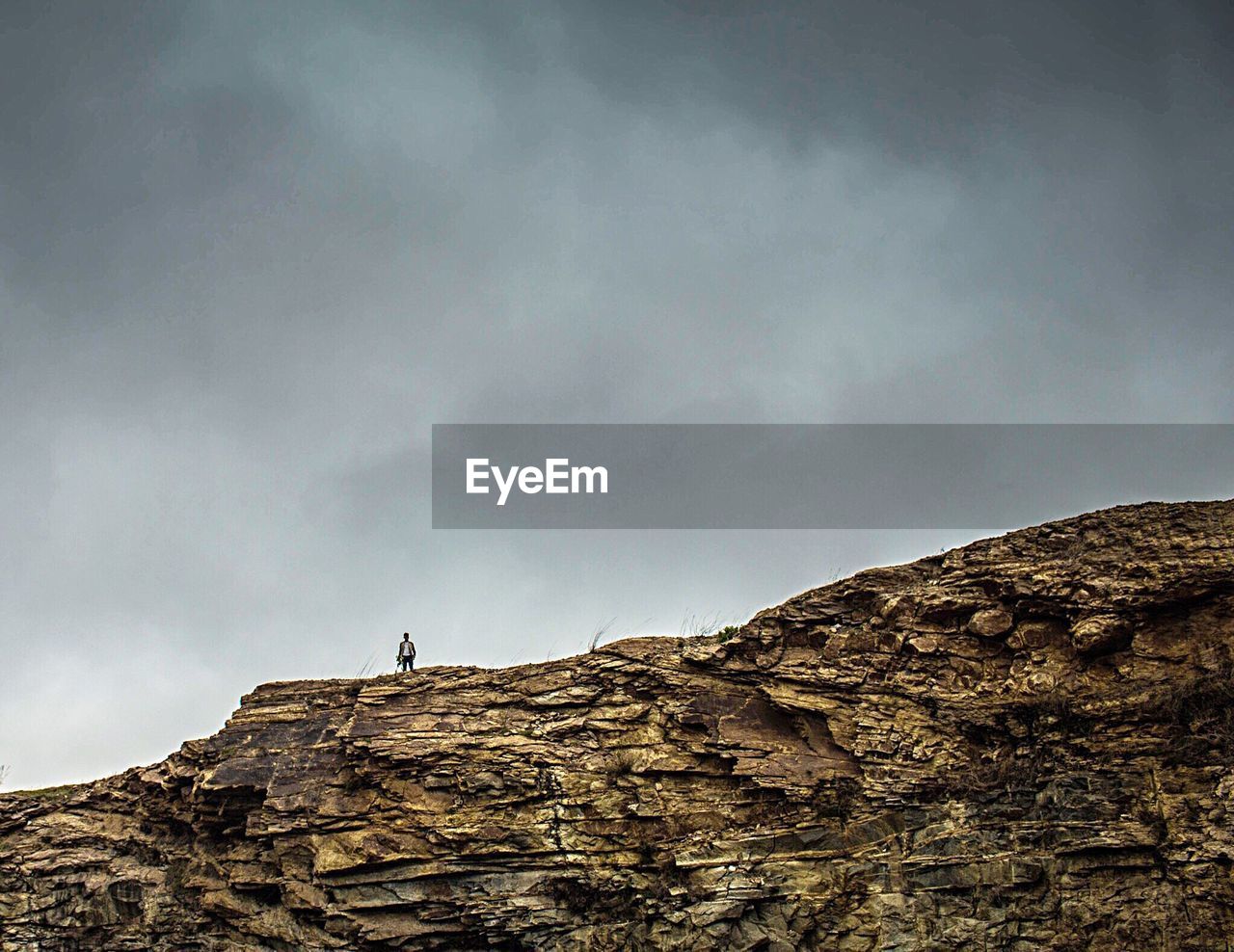 Distant view of man standing on mountain against cloudy sky