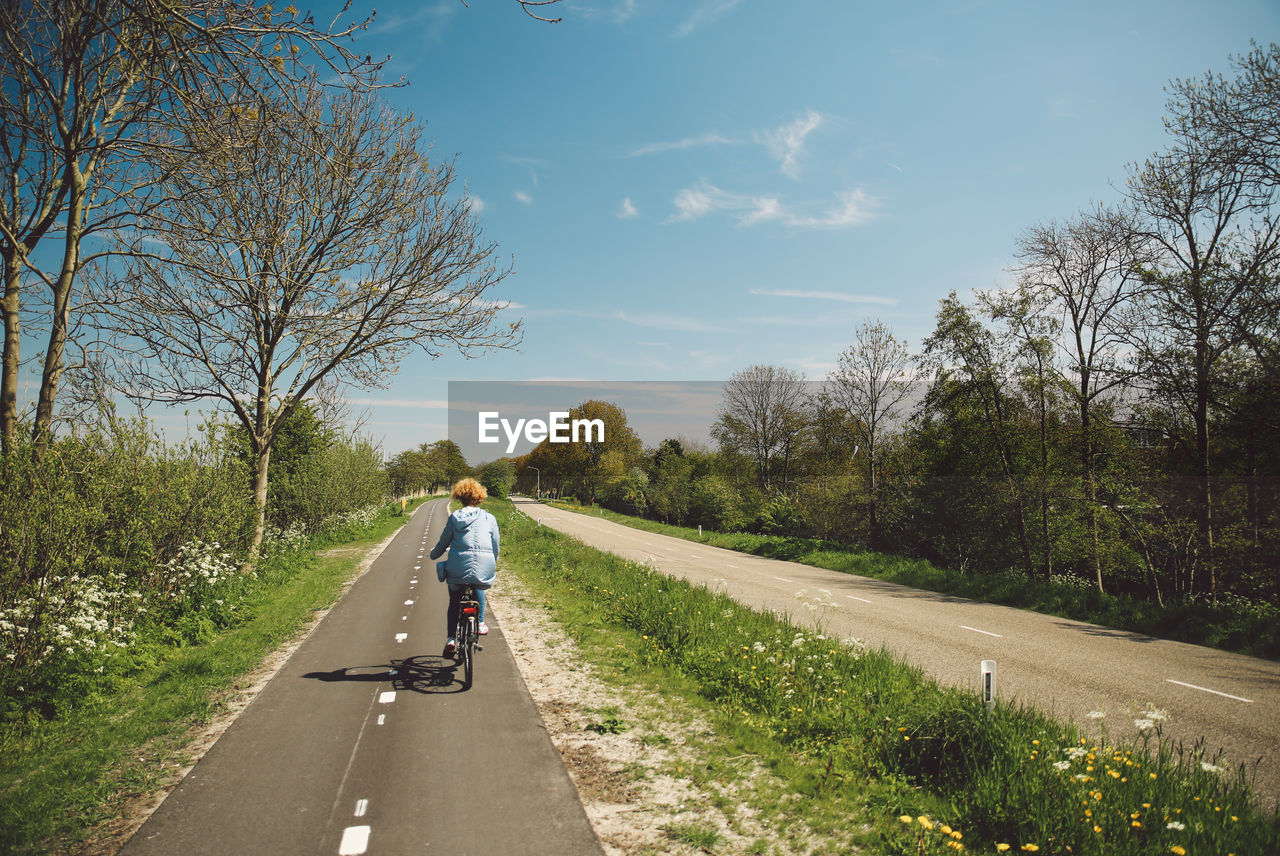 Rear view of woman riding bicycle against sky during sunny day