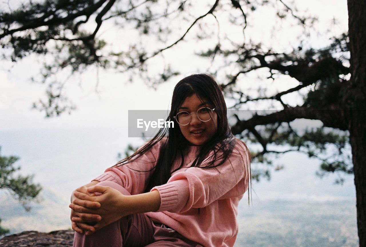 Portrait of young woman standing against trees