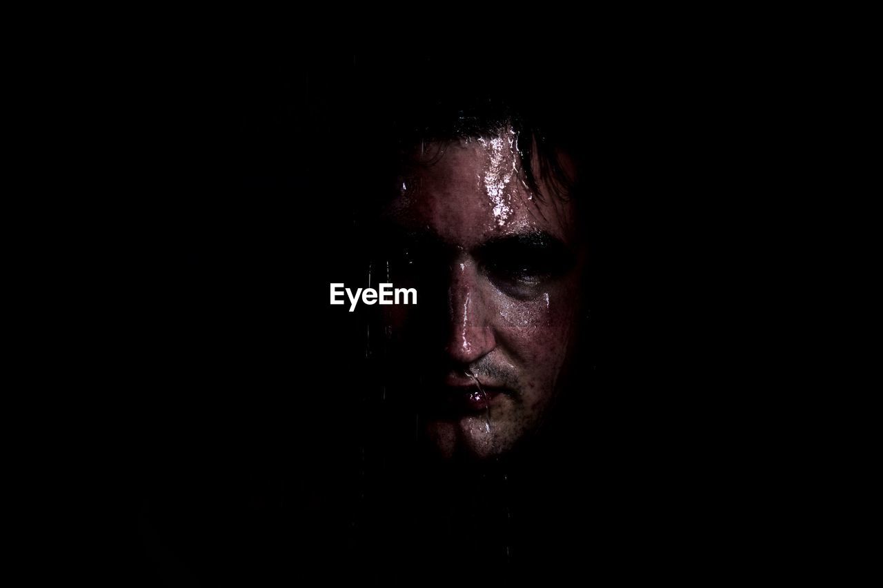 Close-up portrait of mid adult man standing against black background