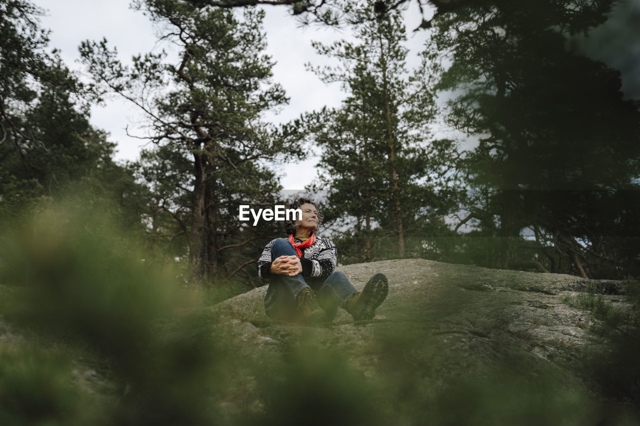 Mature woman sitting on mountain amidst tree in forest