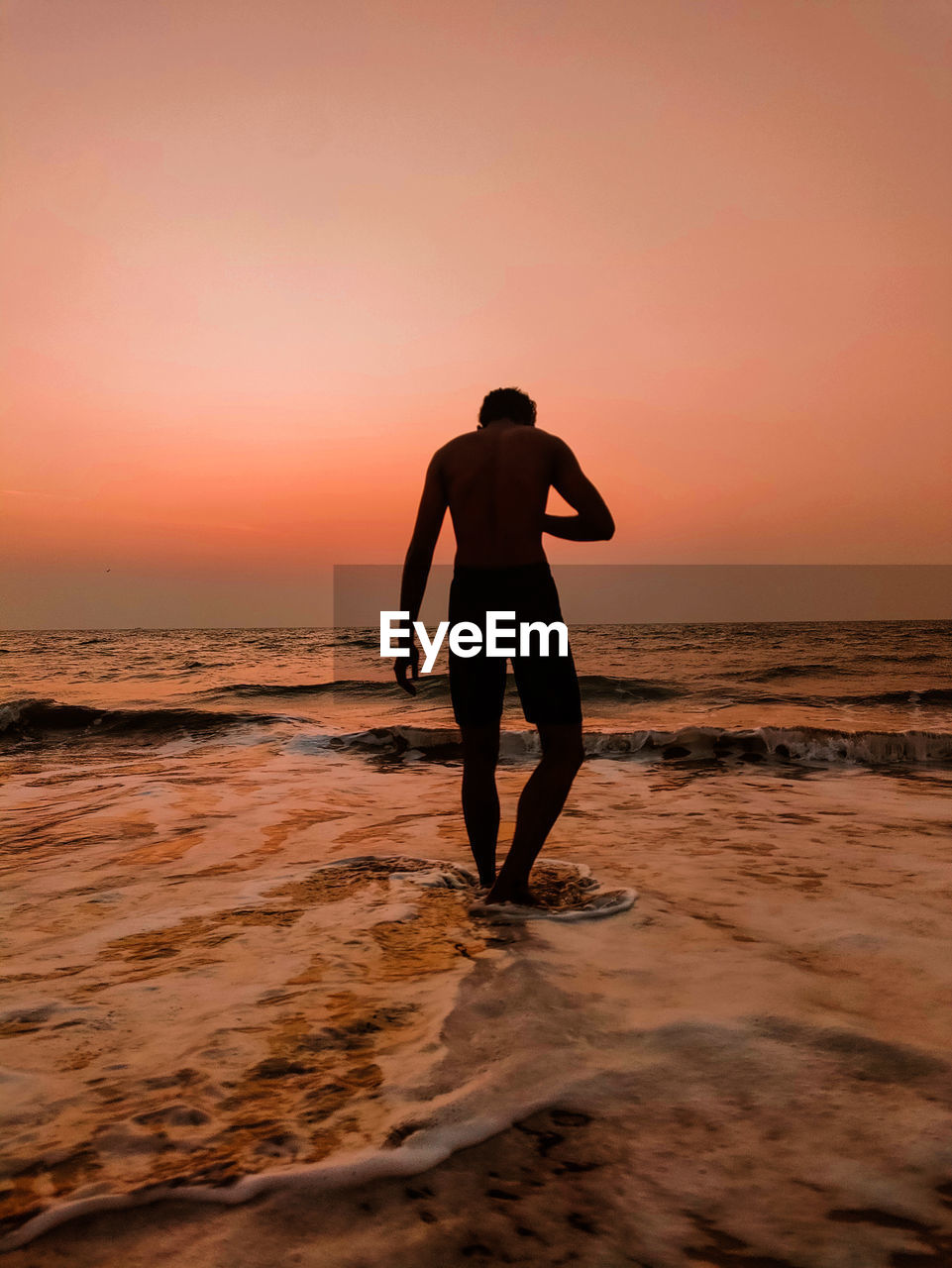 rear view of silhouette woman standing at beach against clear sky during sunset