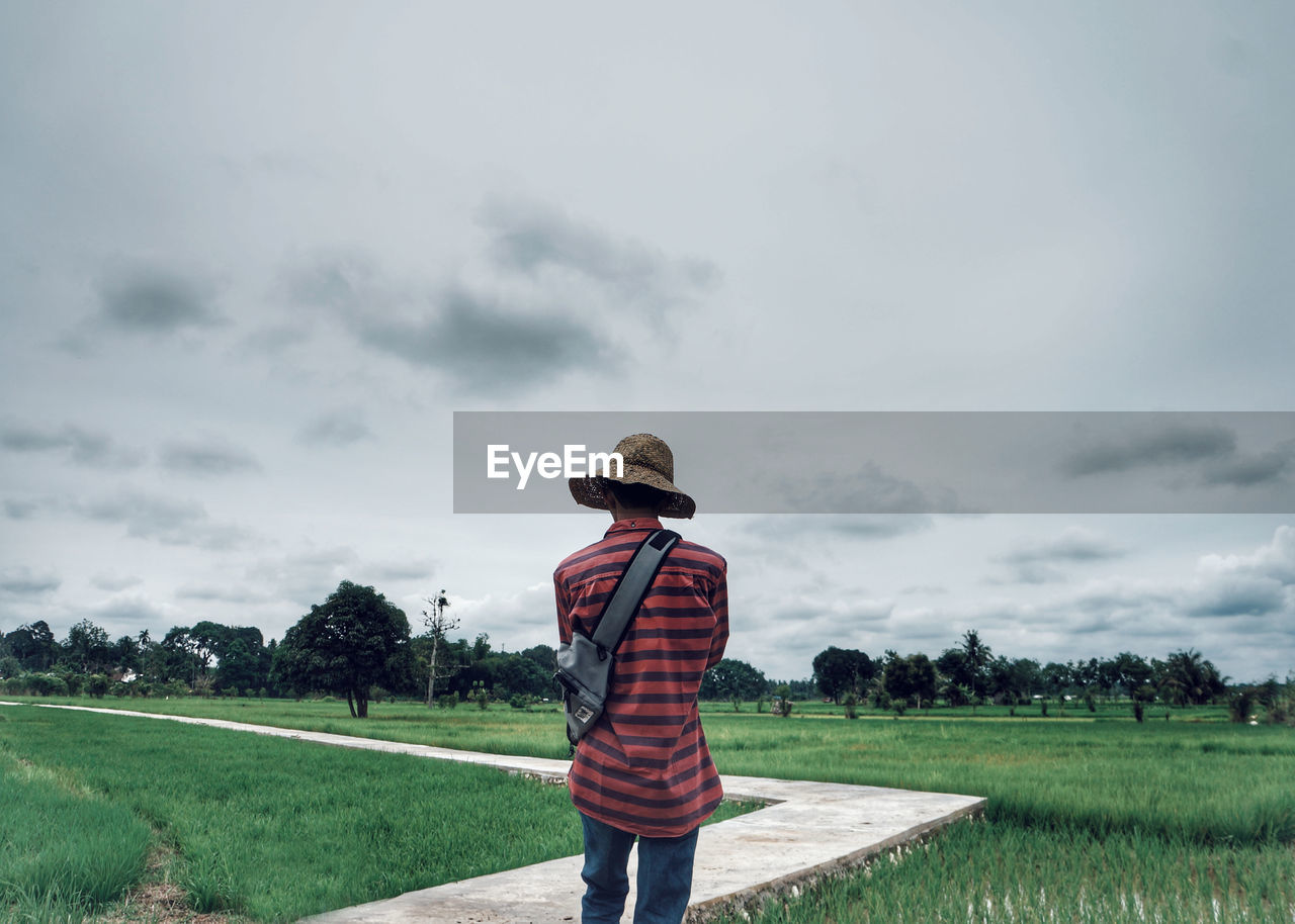 REAR VIEW OF MAN STANDING ON FARM