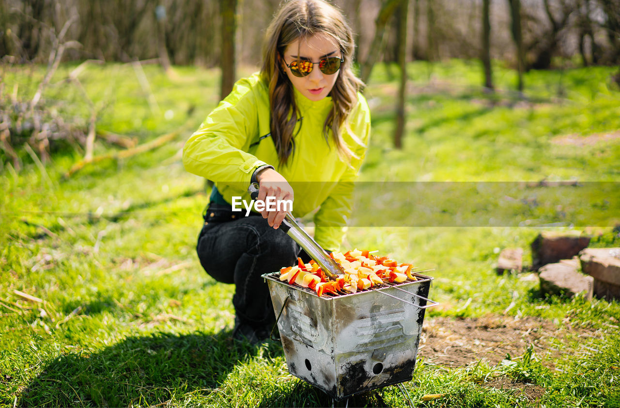 Young woman preparing barbecue skewers in sunny spring day