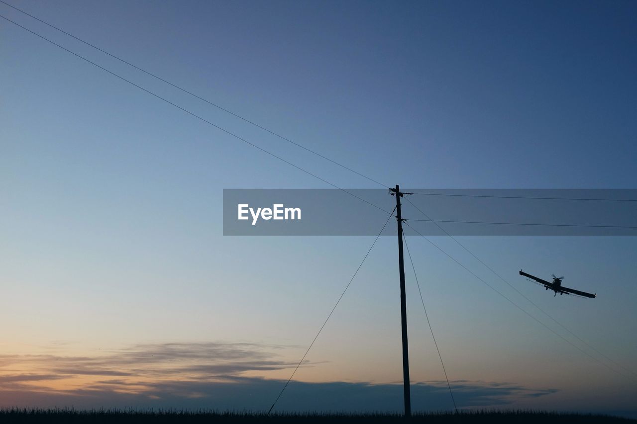 Low angle view of crop sprayer over field against sky during sunset