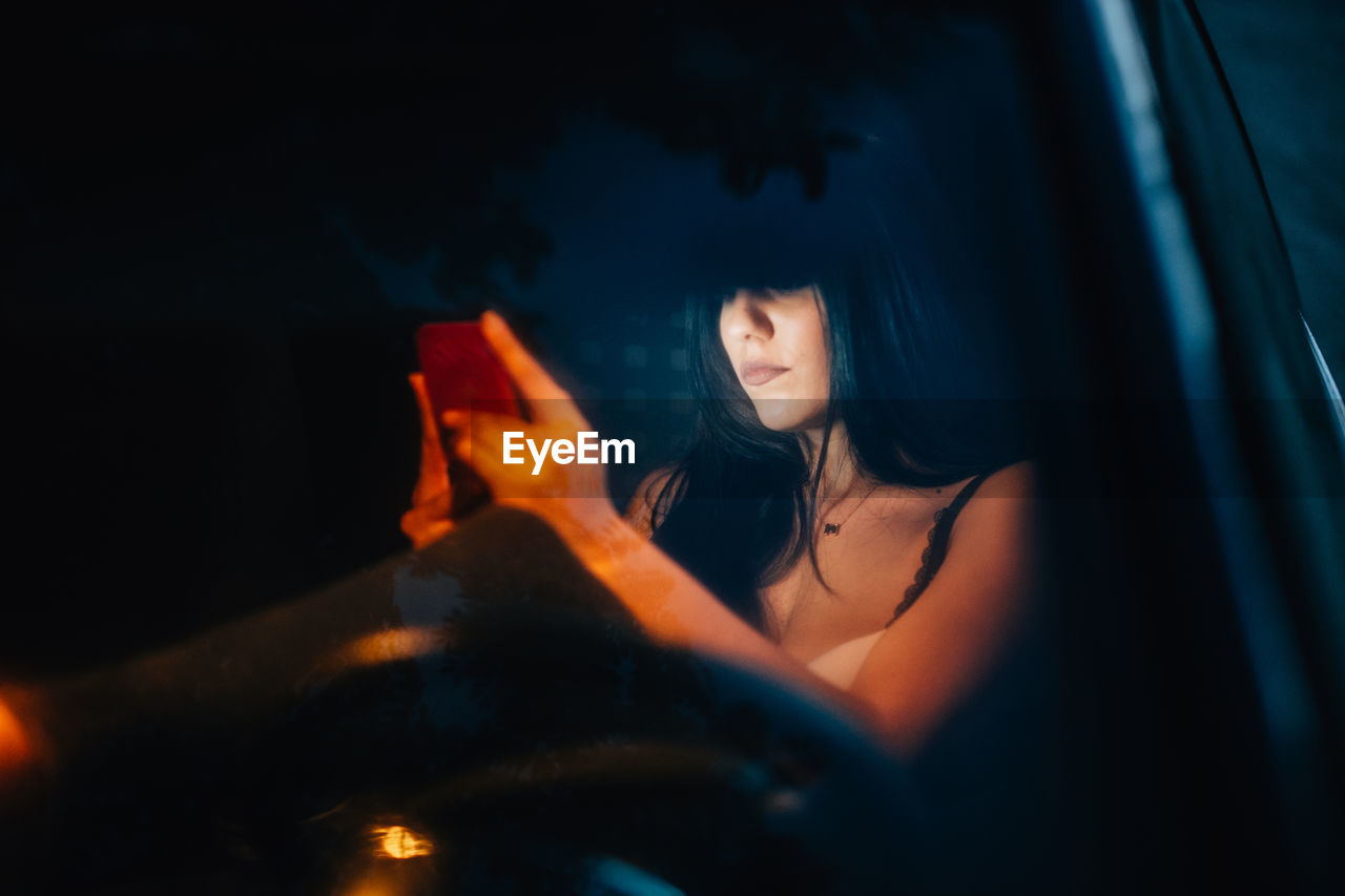Young woman looking at smart phone while sitting in car at night