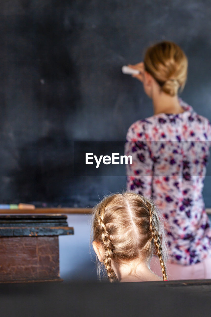 Rear view of teacher teaching female student in classroom