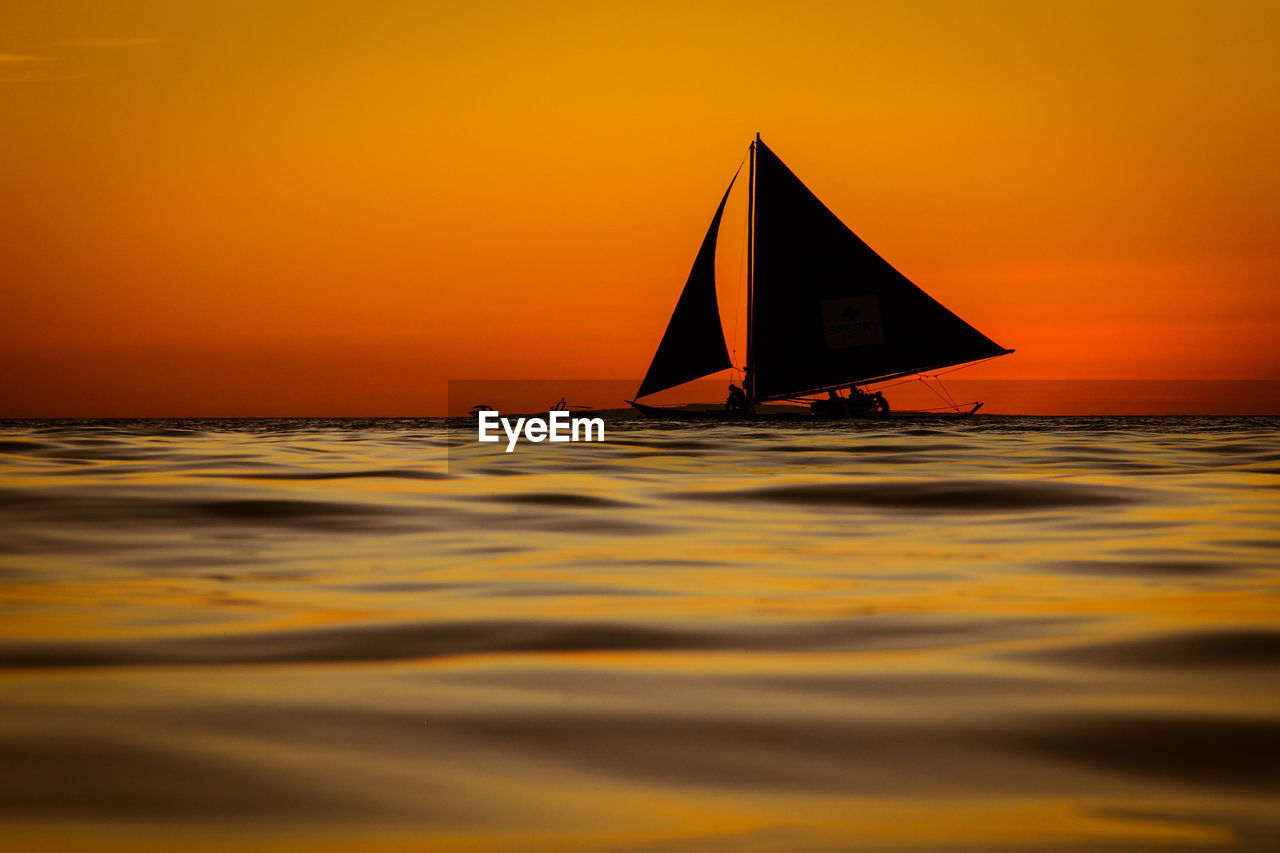 Sailboat in sea against orange sky
