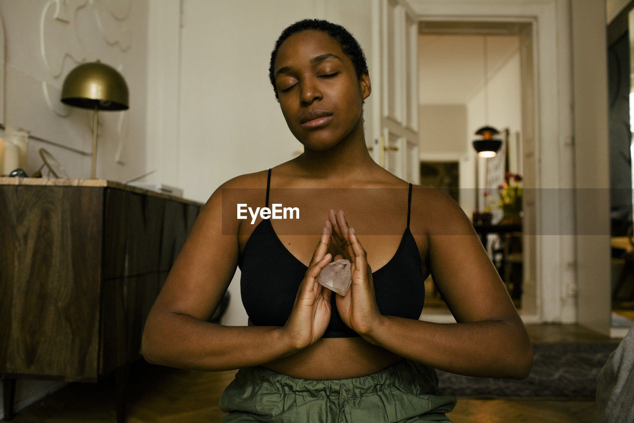 Young woman holding stone while meditating at home