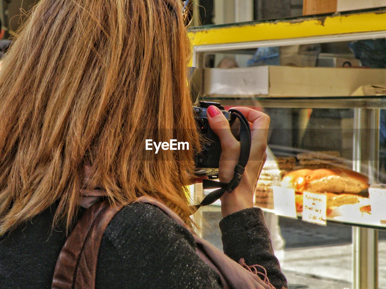 Rear view of woman photographing display cabinet