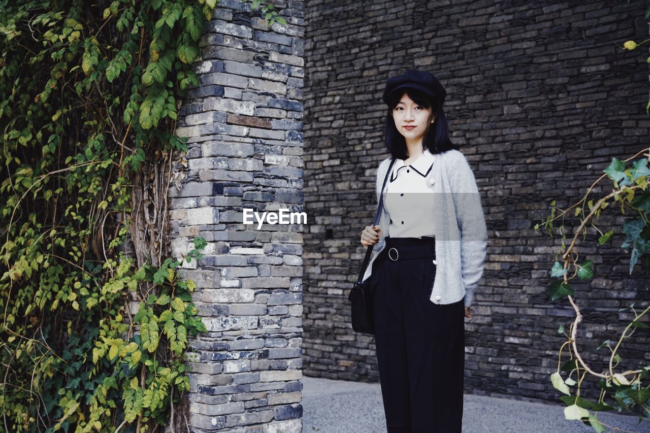 YOUNG WOMAN STANDING AGAINST WALL