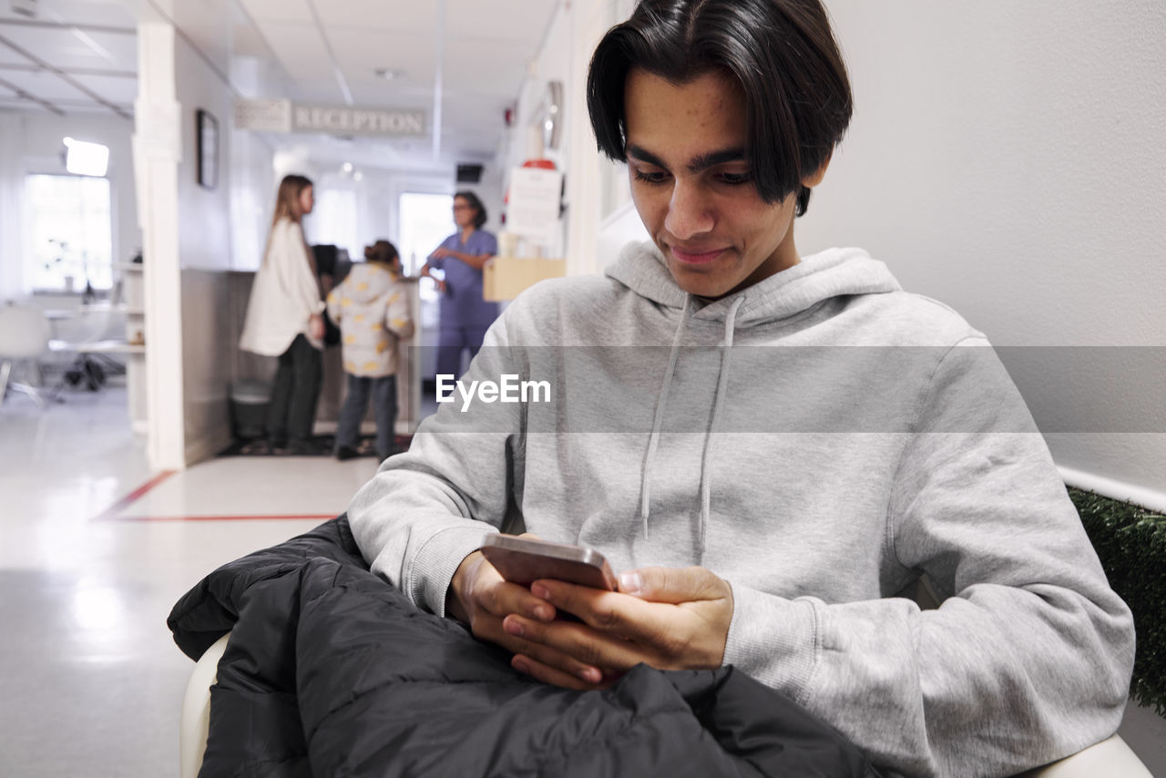 Young male patient waiting in outpatient clinic and using smart phone