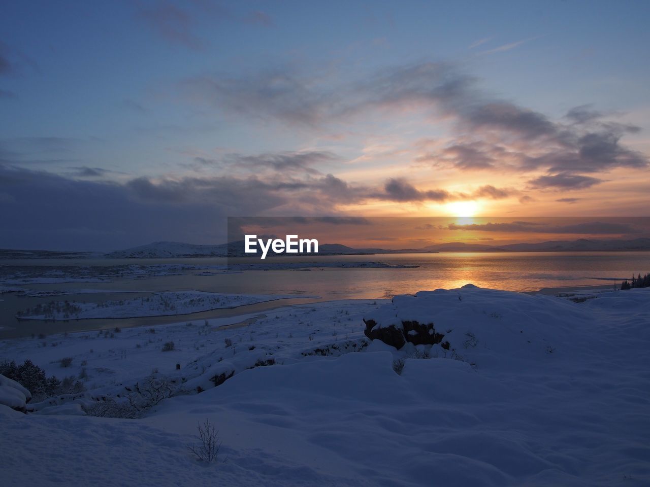 Snow covered landscape against sky during sunset