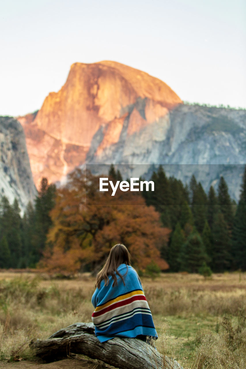 Rear view of woman sitting on field against mountain