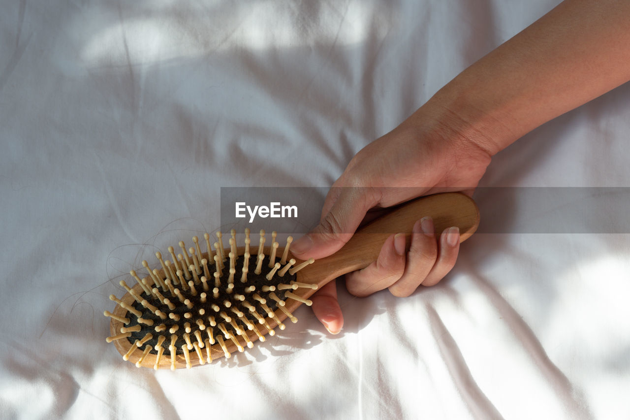 Cropped hand holding hairbrush on bed