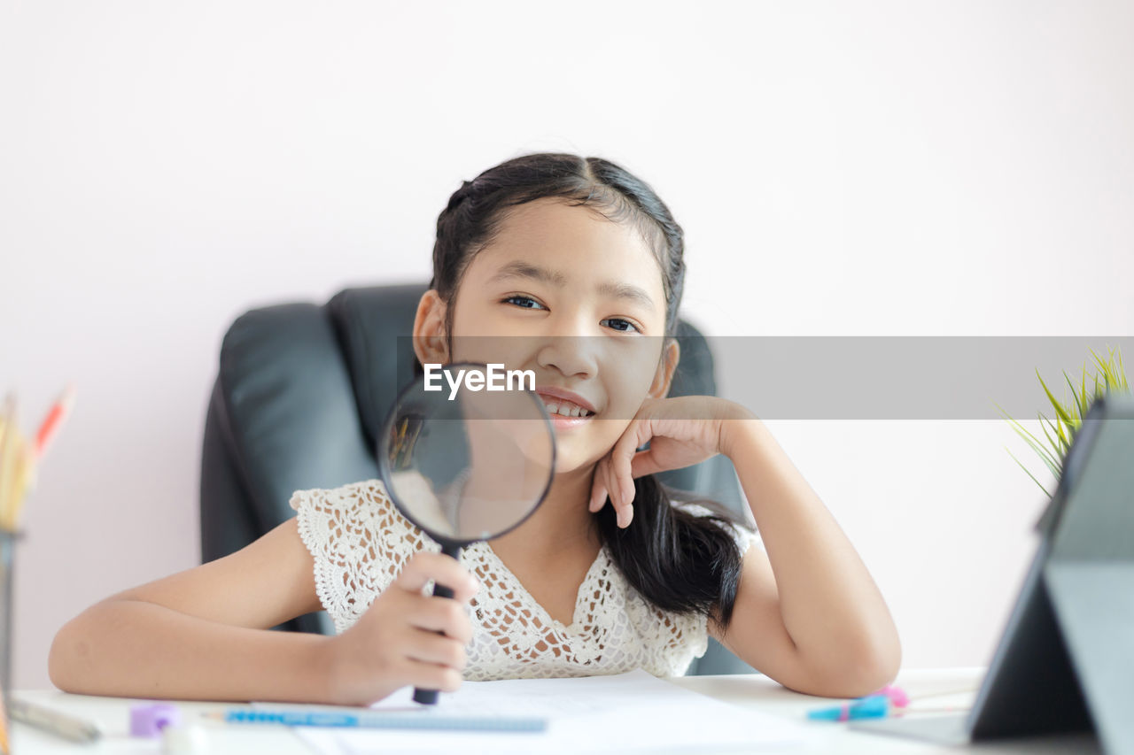 Portrait of cute girl holding magnifying glass against white background