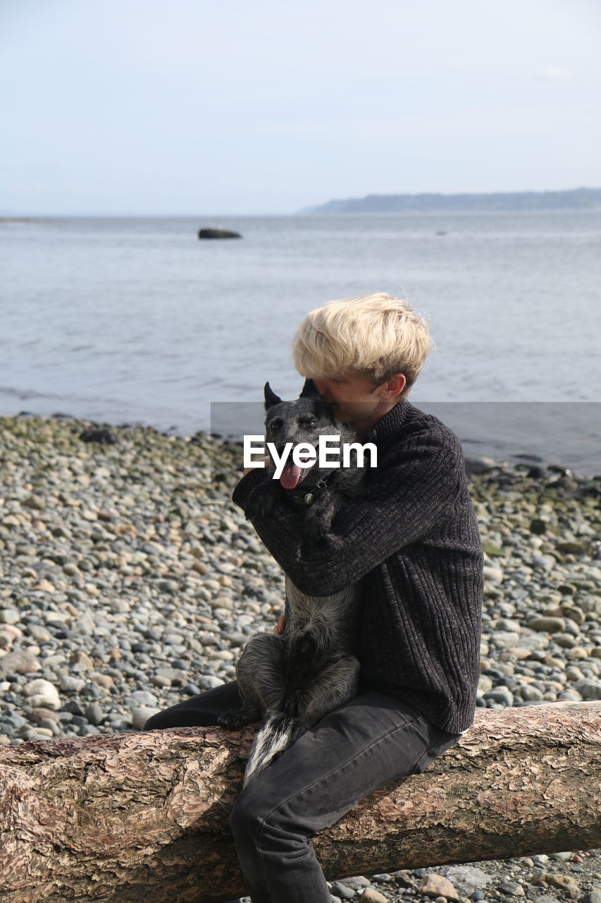 Young man embracing dog while sitting by lakeshore