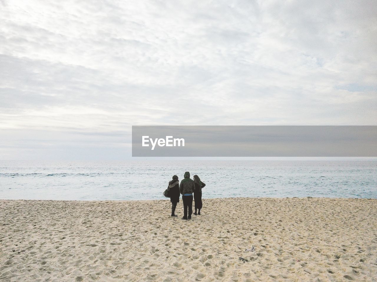 REAR VIEW OF MEN STANDING AT BEACH