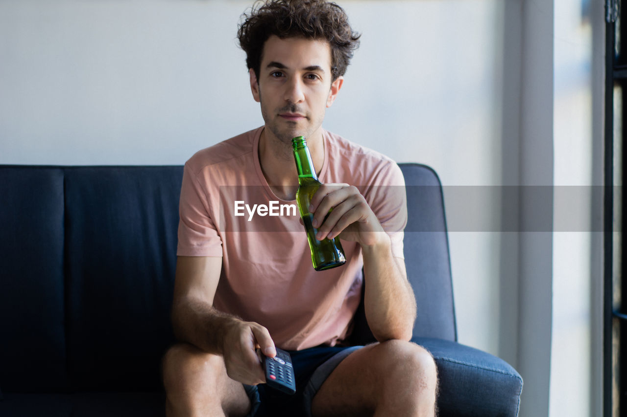 PORTRAIT OF YOUNG MAN SITTING AGAINST SEAT