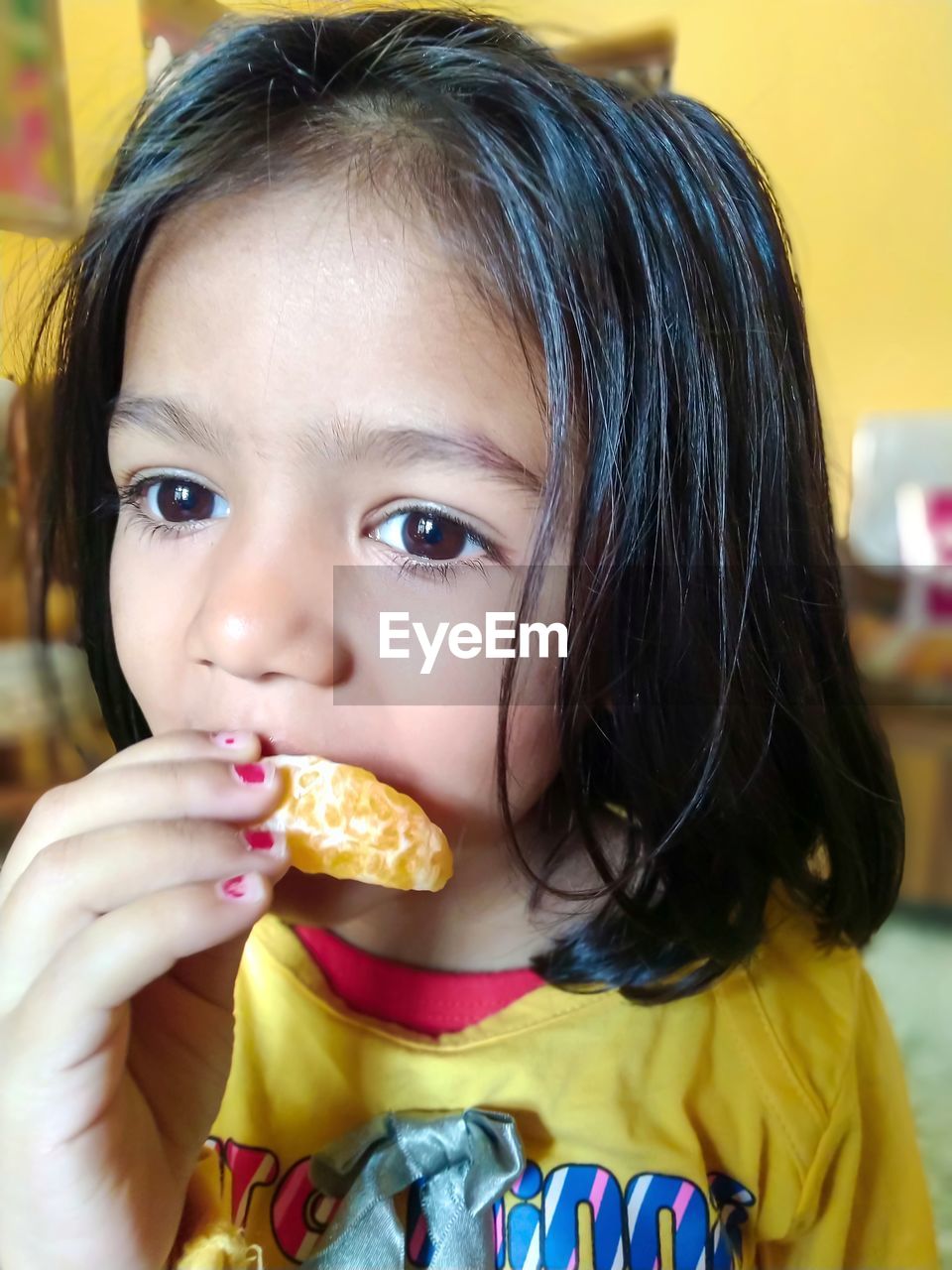 Close-up of innocent girl eating orange fruit at home