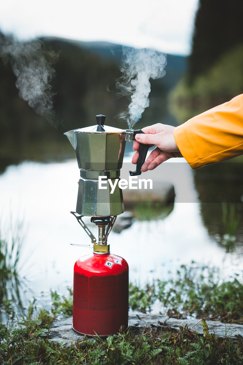 Cropped hand holding coffee maker on camping stove